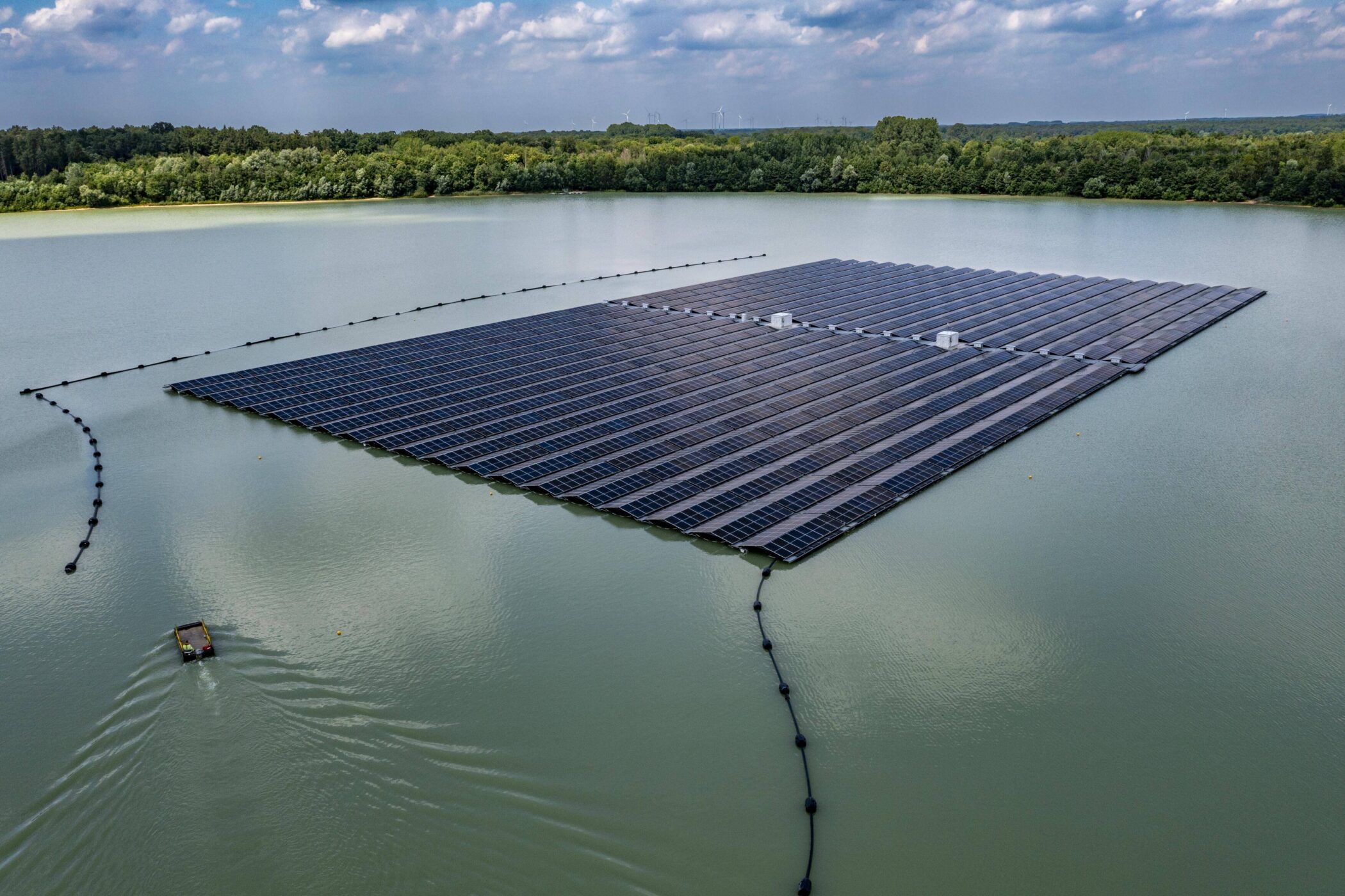 Schwimmende Solaranlage auf einem See, umgeben von Wald. Ein Boot auf dem Wasser.