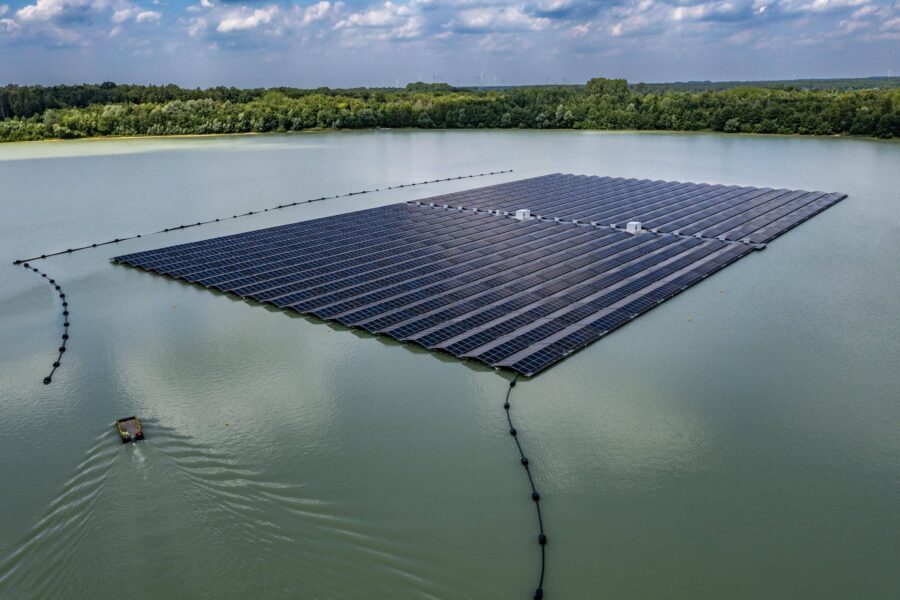 Schwimmende Solaranlage auf einem See, umgeben von Wald. Ein Boot auf dem Wasser.