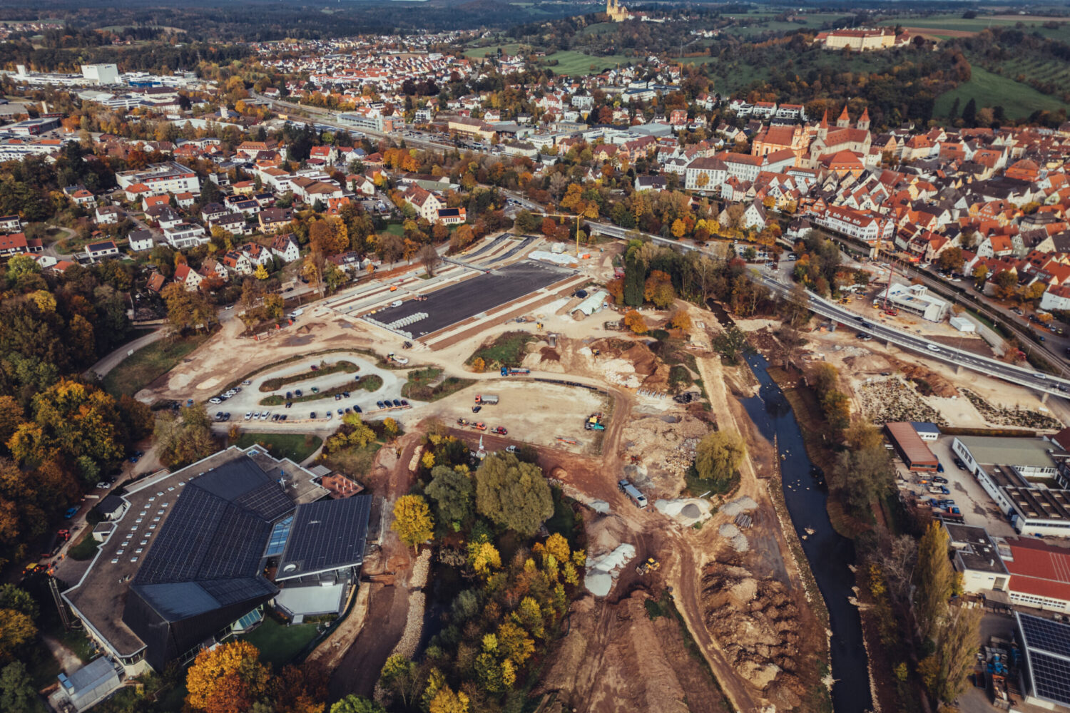Luftaufnahme einer Stadt mit Baustelle, Fluss und umliegenden Gebäuden.