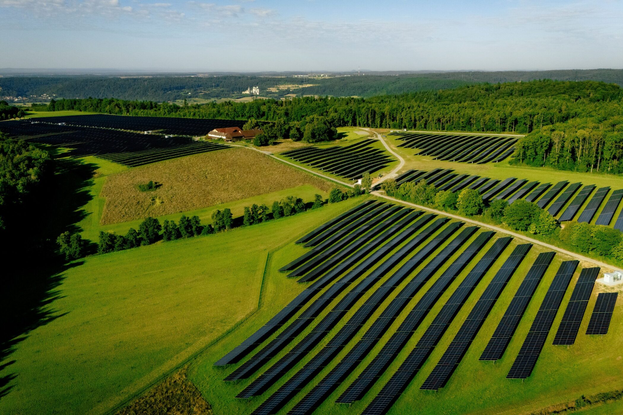 Weitläufige Solaranlage auf grünen Feldern, umgeben von Wäldern.