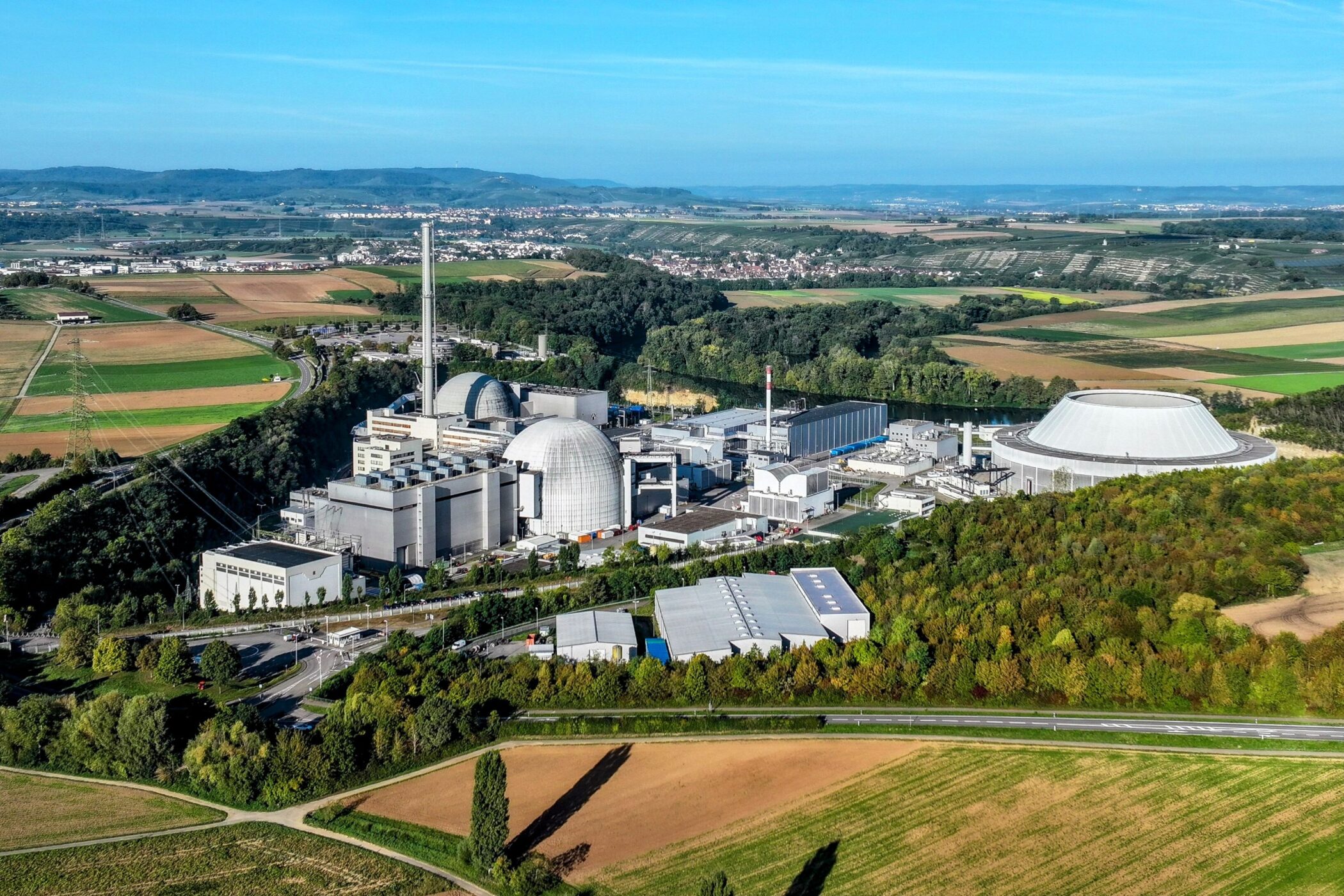 Industrieanlage mit großen Kuppeln und Schornstein, umgeben von Feldern und Wäldern.