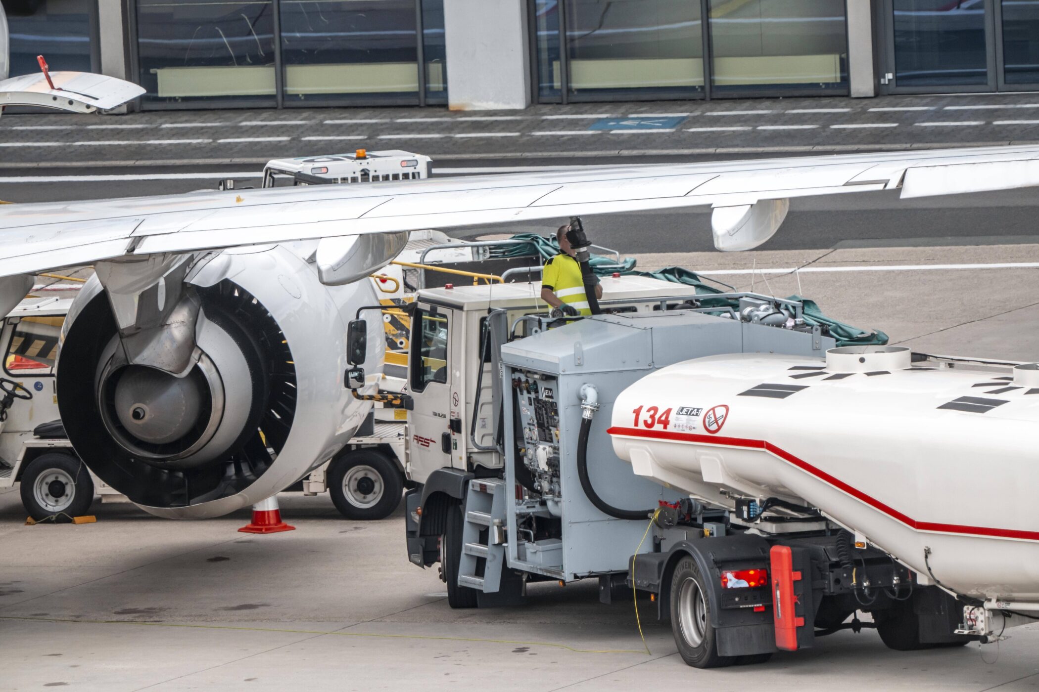 Flugzeugbetankung am Flughafen, Person in Warnweste, Tankfahrzeug neben Triebwerk.
