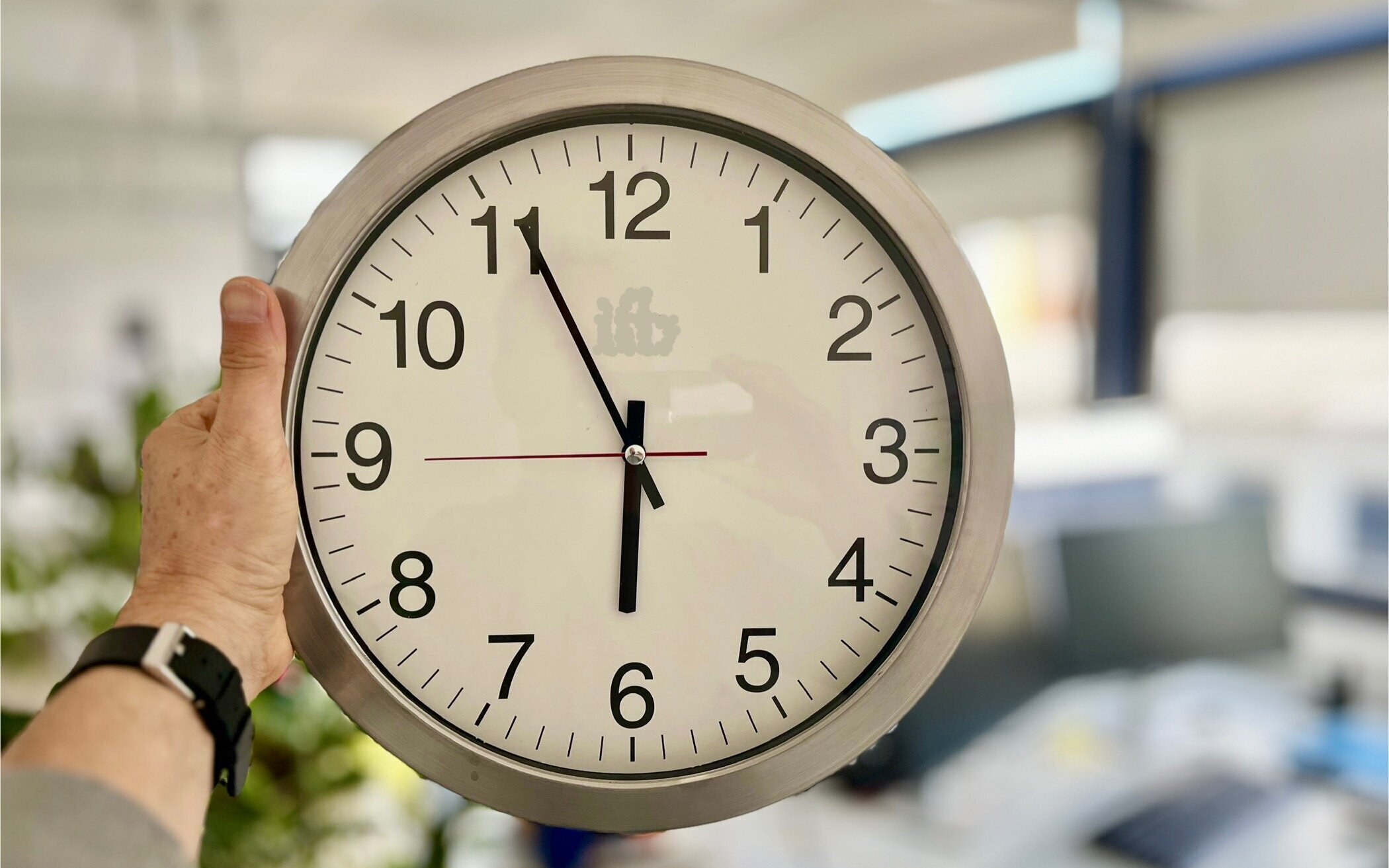 Eine Hand hält eine analoge Uhr, die 10:10 Uhr zeigt.