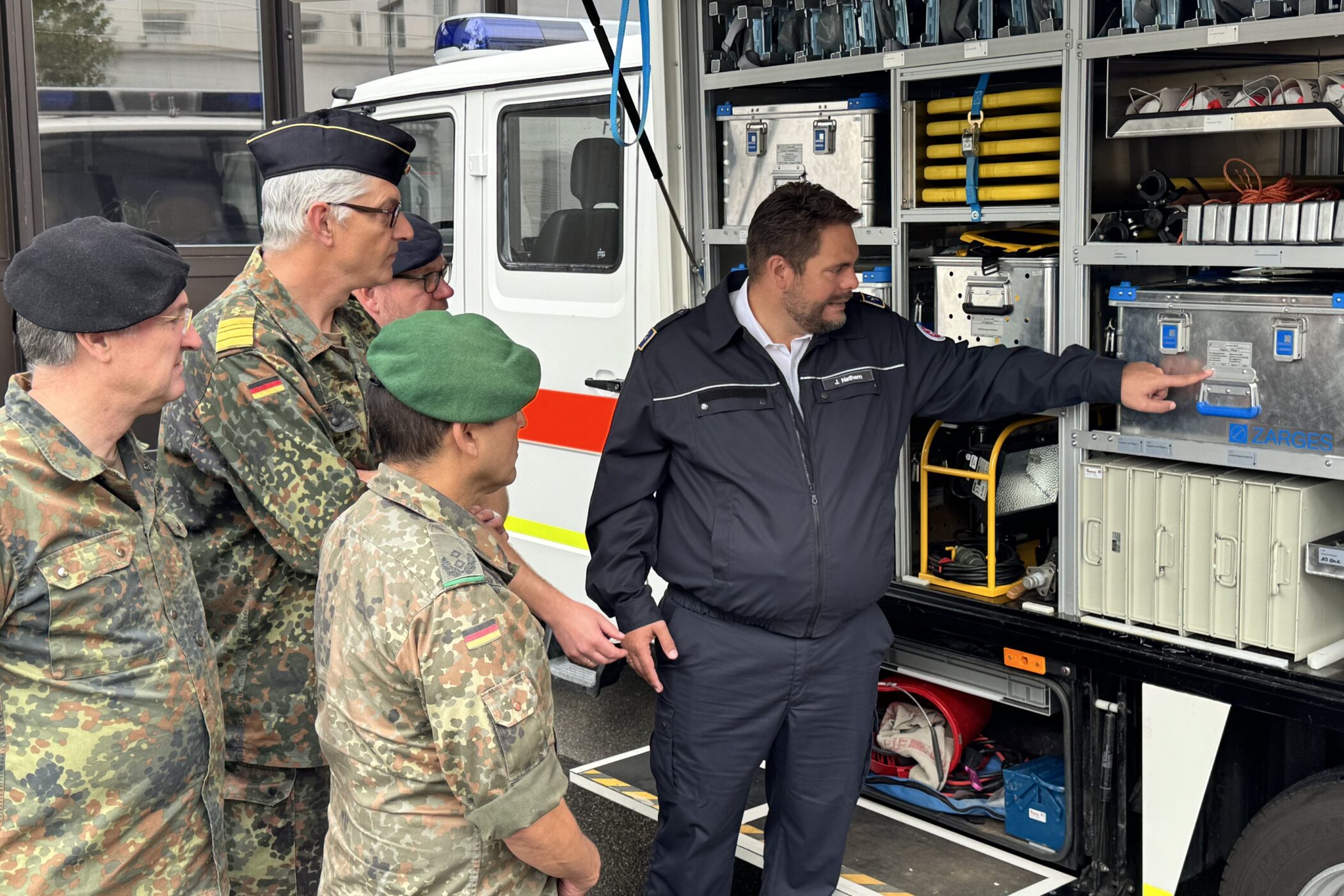Fünf Personen in Uniformen vor einem geöffneten Einsatzfahrzeug.