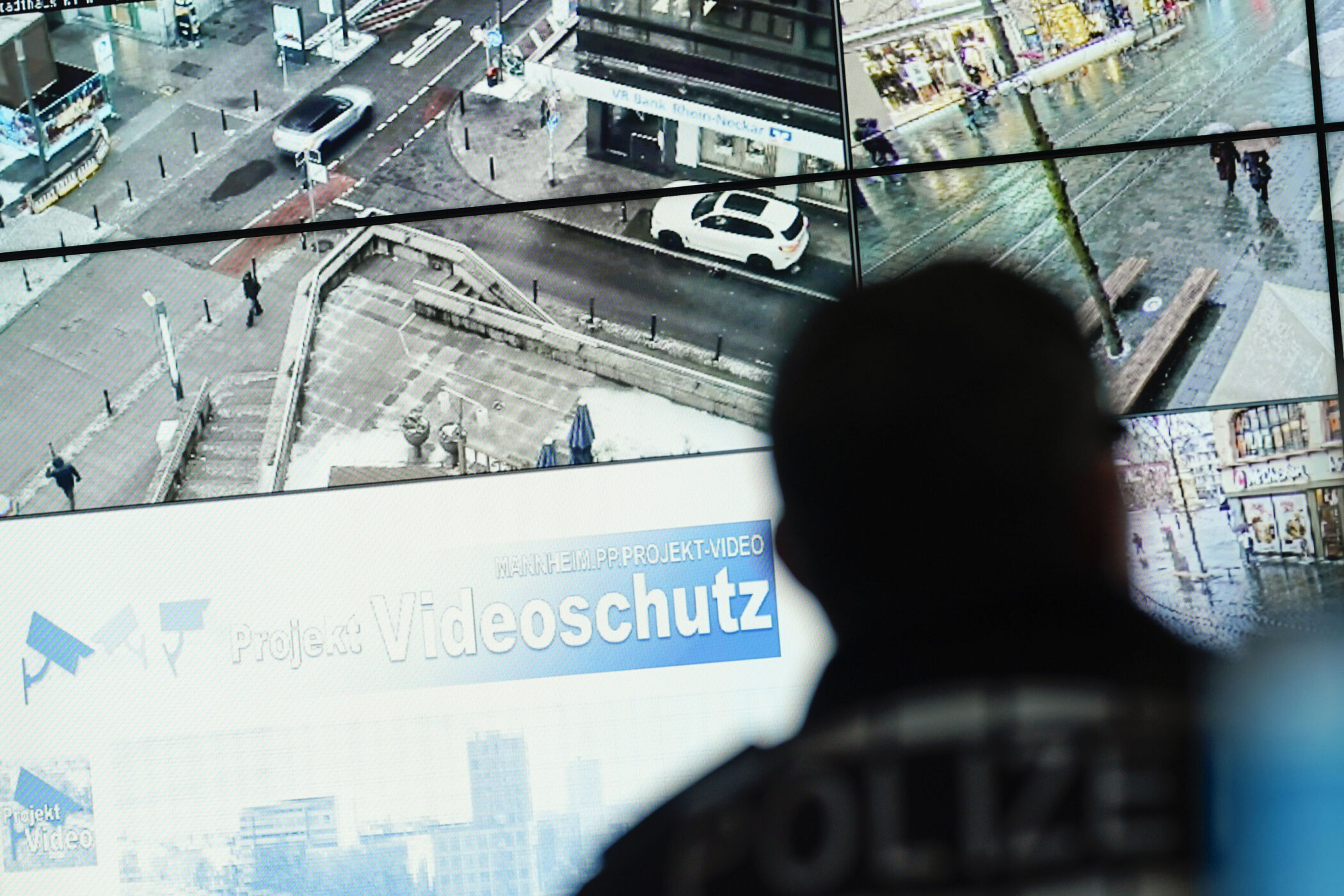 Person vor Überwachungsmonitoren mit Stadtansichten, Text: "Videoschutz".