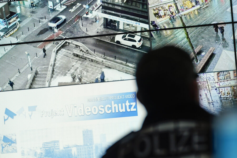 Person vor Überwachungsmonitoren mit Stadtansichten, Text: "Videoschutz".