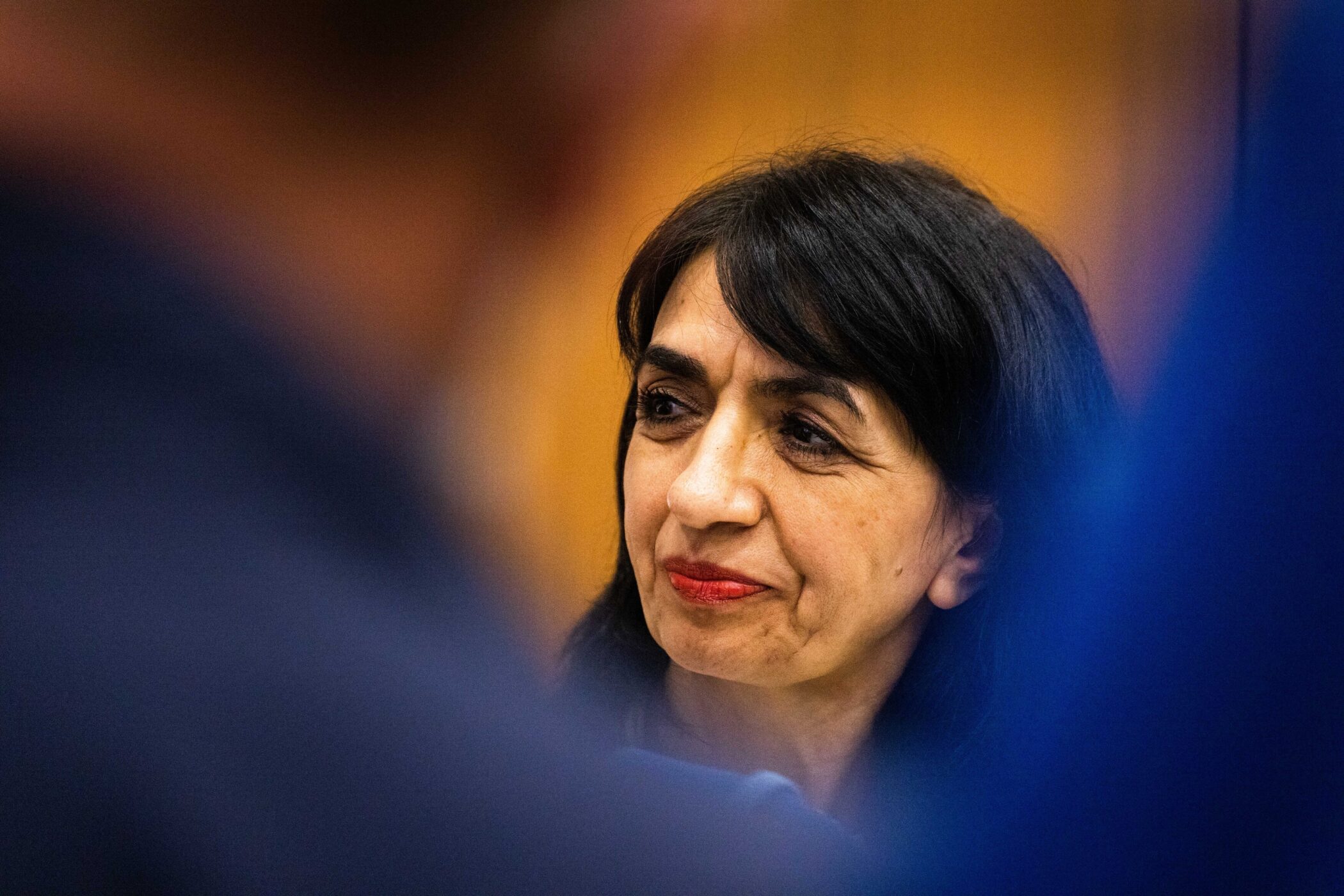 Frau mit dunklem Haar und rotem Lippenstift, unscharfer Vordergrund.