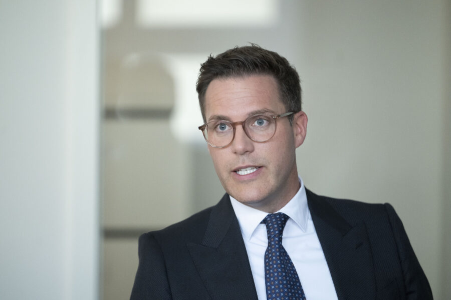 Mann mit Brille und Anzug spricht, unscharfer Hintergrund.