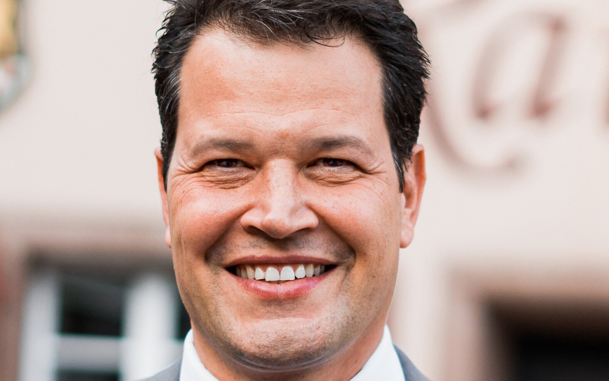 Lächelnder Mann in Anzug vor unscharfem Hintergrund.