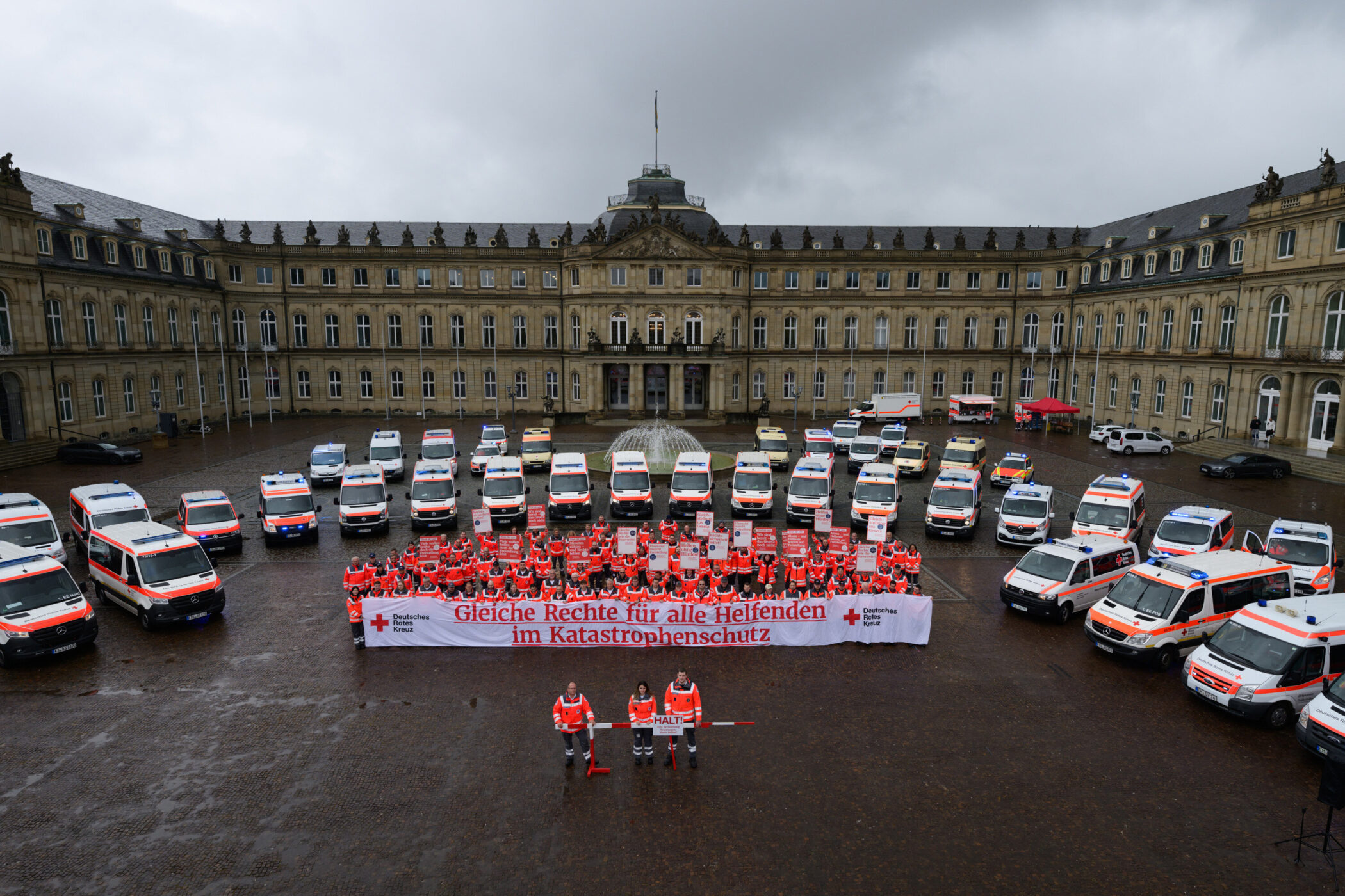 Viele Menschen in roten Uniformen vor Rettungsfahrzeugen und einem großen Gebäude.