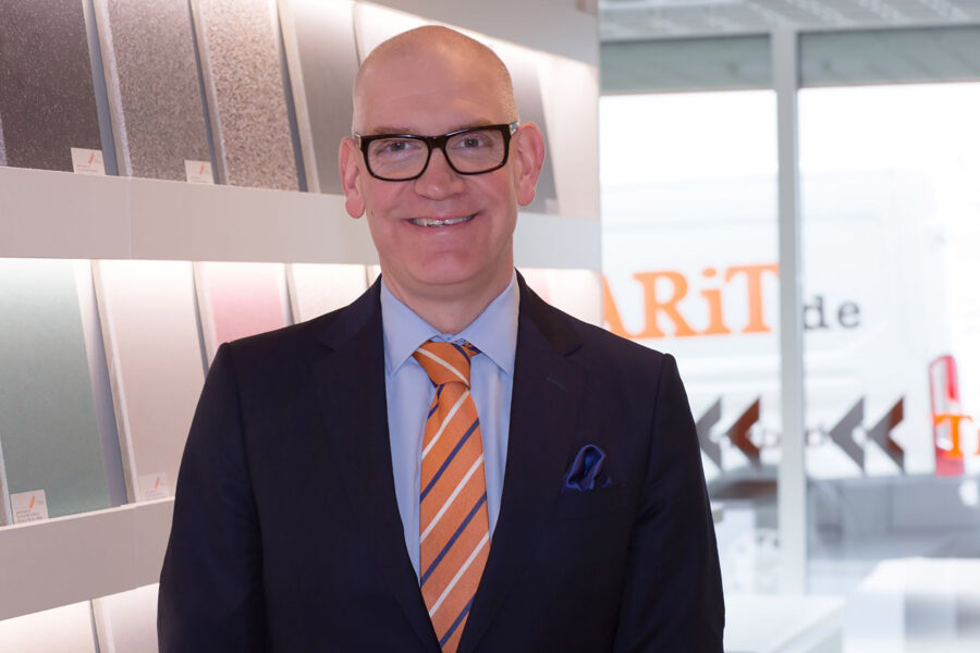 Mann mit Brille und Anzug steht vor einer Wand mit Farbmusterplatten.