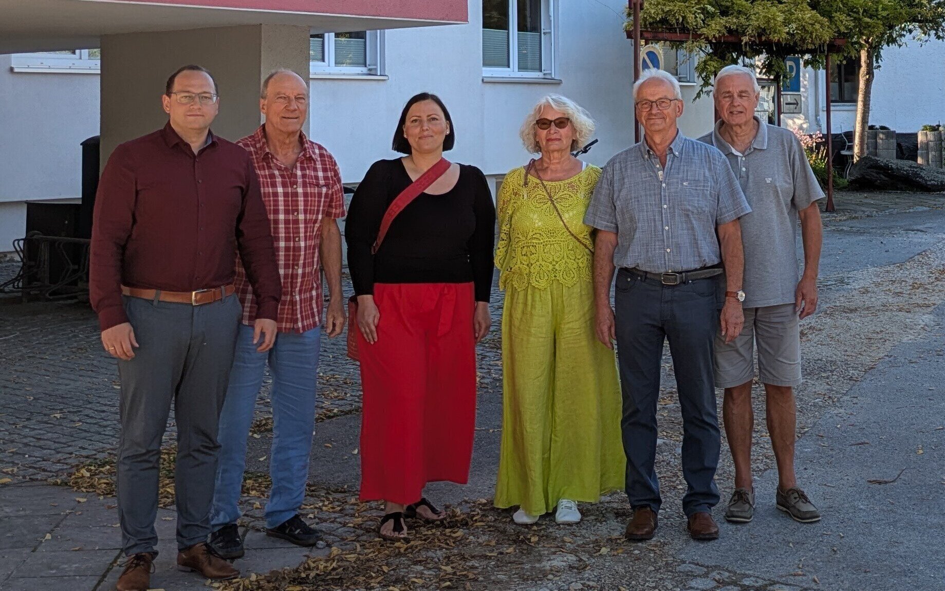 Sechs Personen stehen nebeneinander auf einem Gehweg vor einem Gebäude.