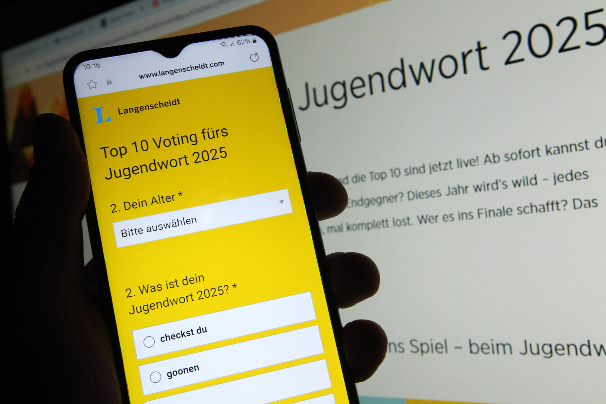 Smartphone zeigt Voting-Seite für Jugendwort 2025, Hintergrund unscharf.