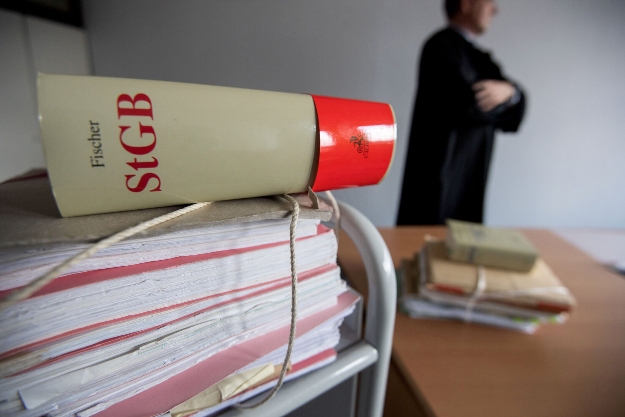 Aktenstapel mit Buch "Fischer StGB", unscharfe Person im Hintergrund.
