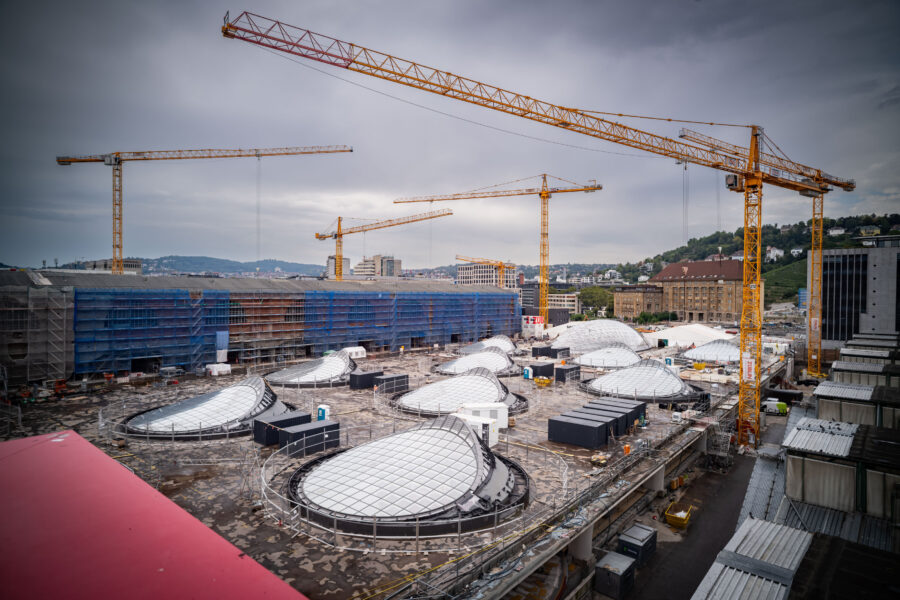 Baustelle mit mehreren Kränen und kuppelförmigen Strukturen auf einem Dach.