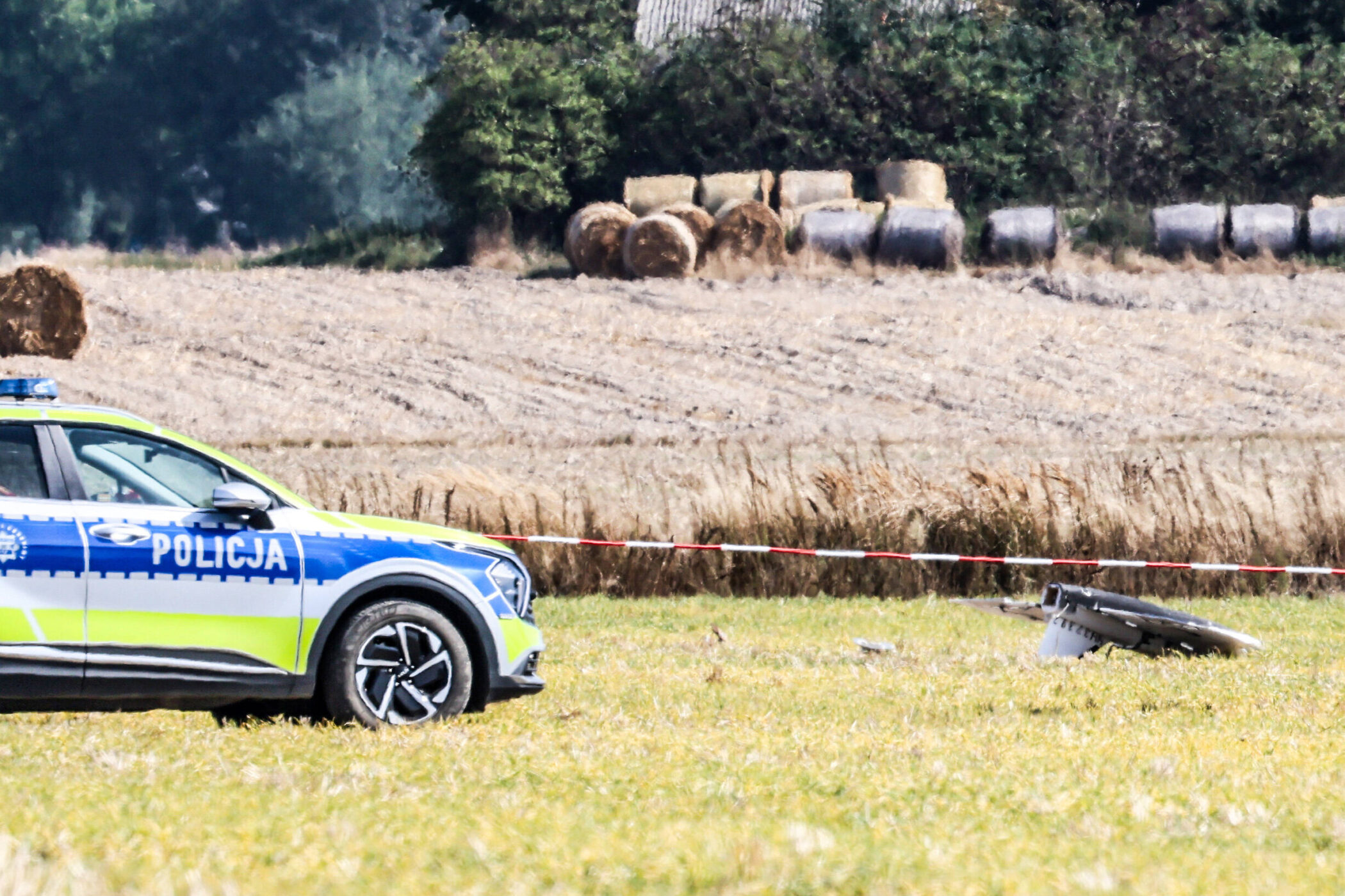 Polizeiauto auf Feld, Absperrband, Strohballen im Hintergrund.