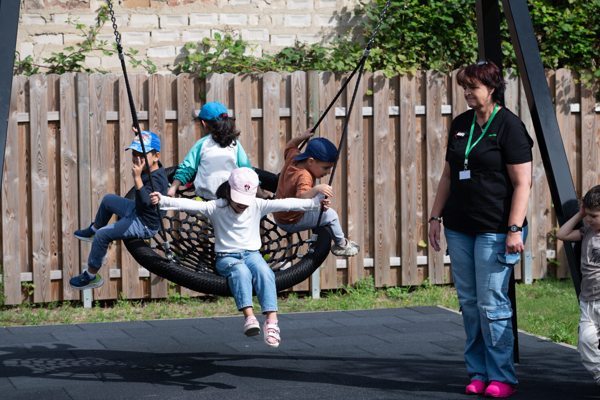 Vier Kinder schaukeln auf einer Netzschaukel, Frau steht daneben.