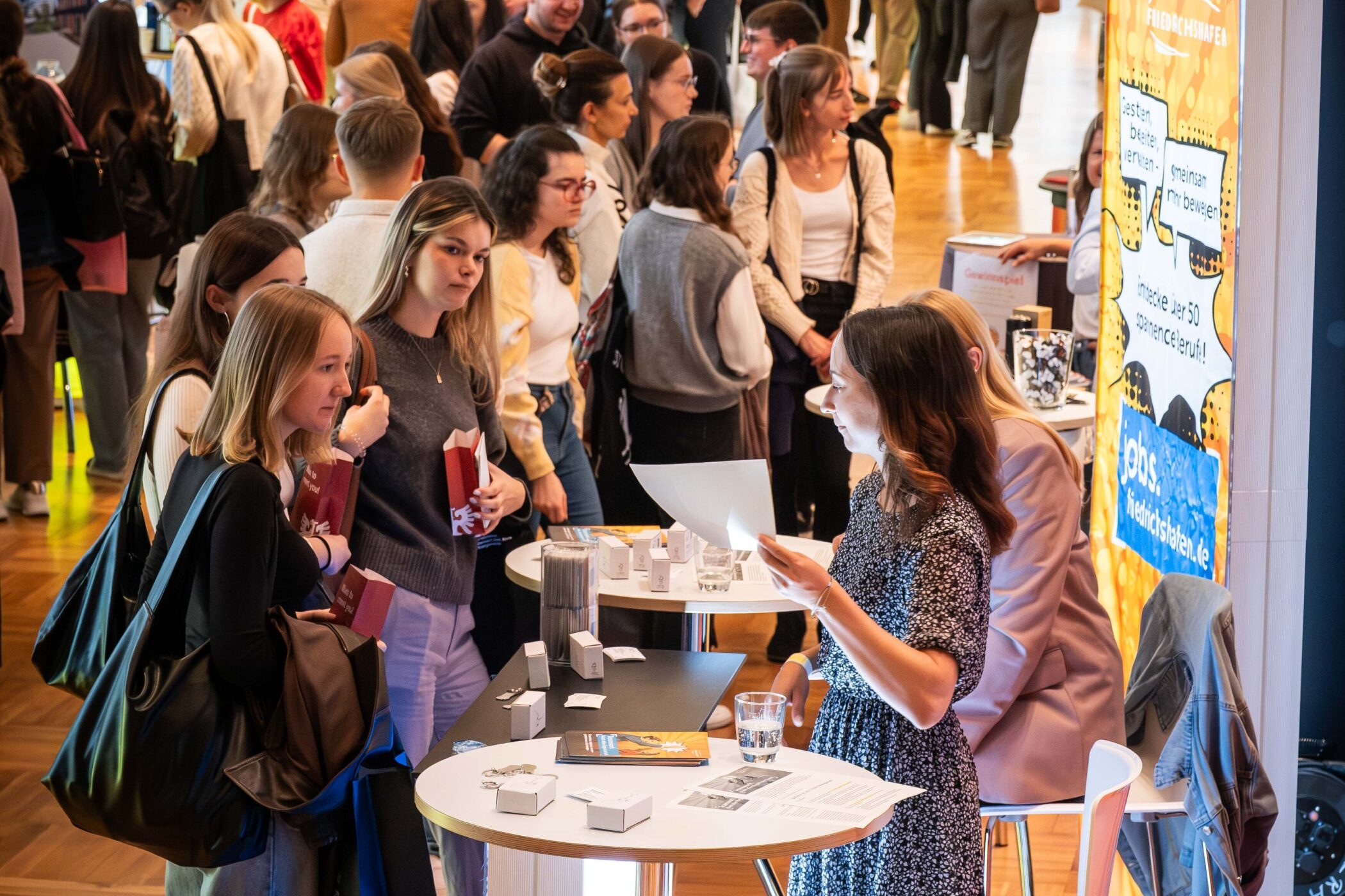 Menschenmenge bei einer Messe, mehrere Stände und Informationsmaterial.