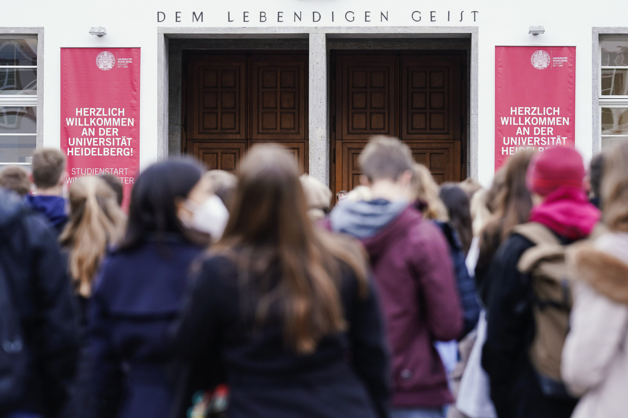 Gruppe von Menschen vor einem Gebäude mit Willkommenstext der Universität Heidelberg.