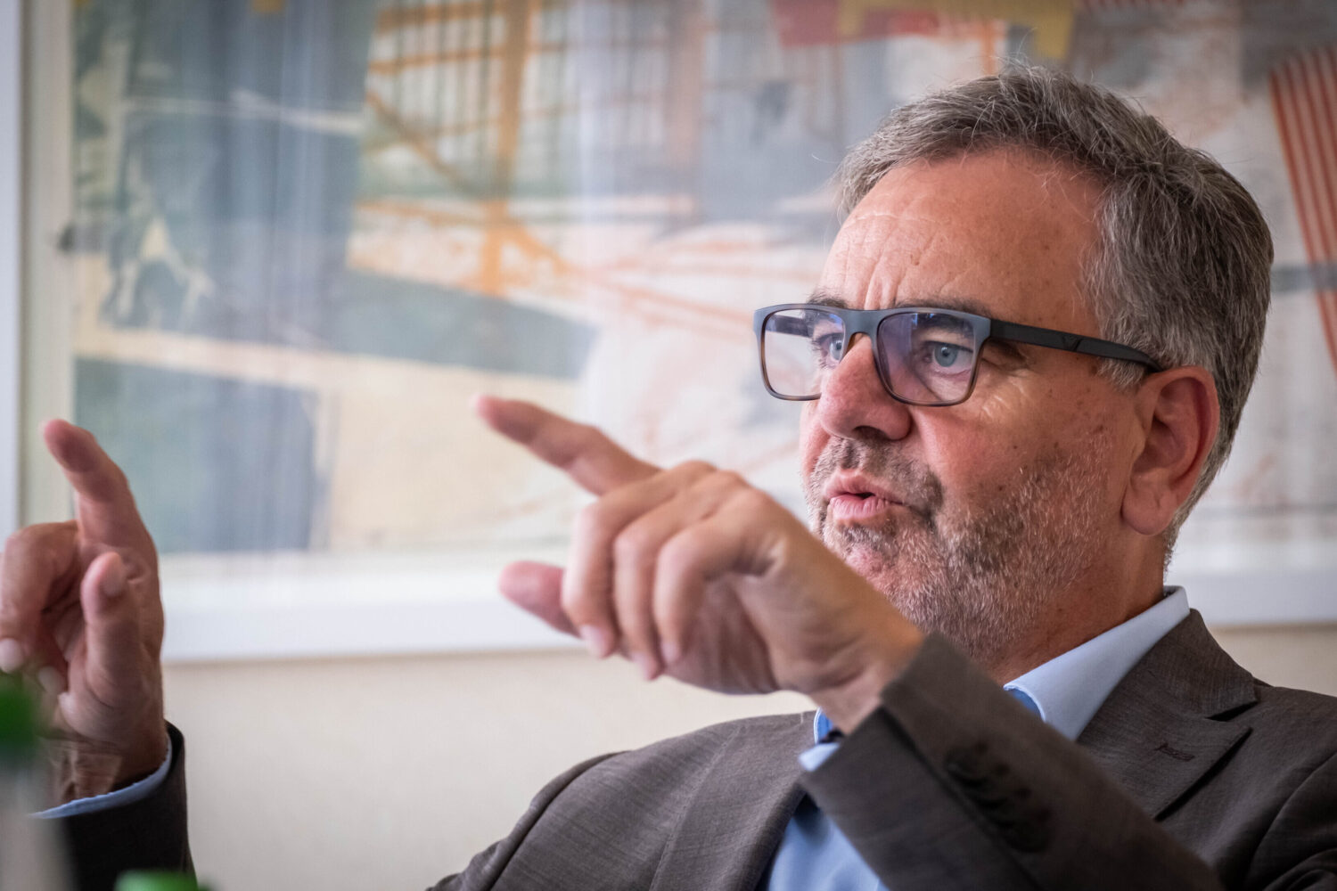 Mann mit Brille gestikuliert, unscharfer Hintergrund mit Kunstwerk.