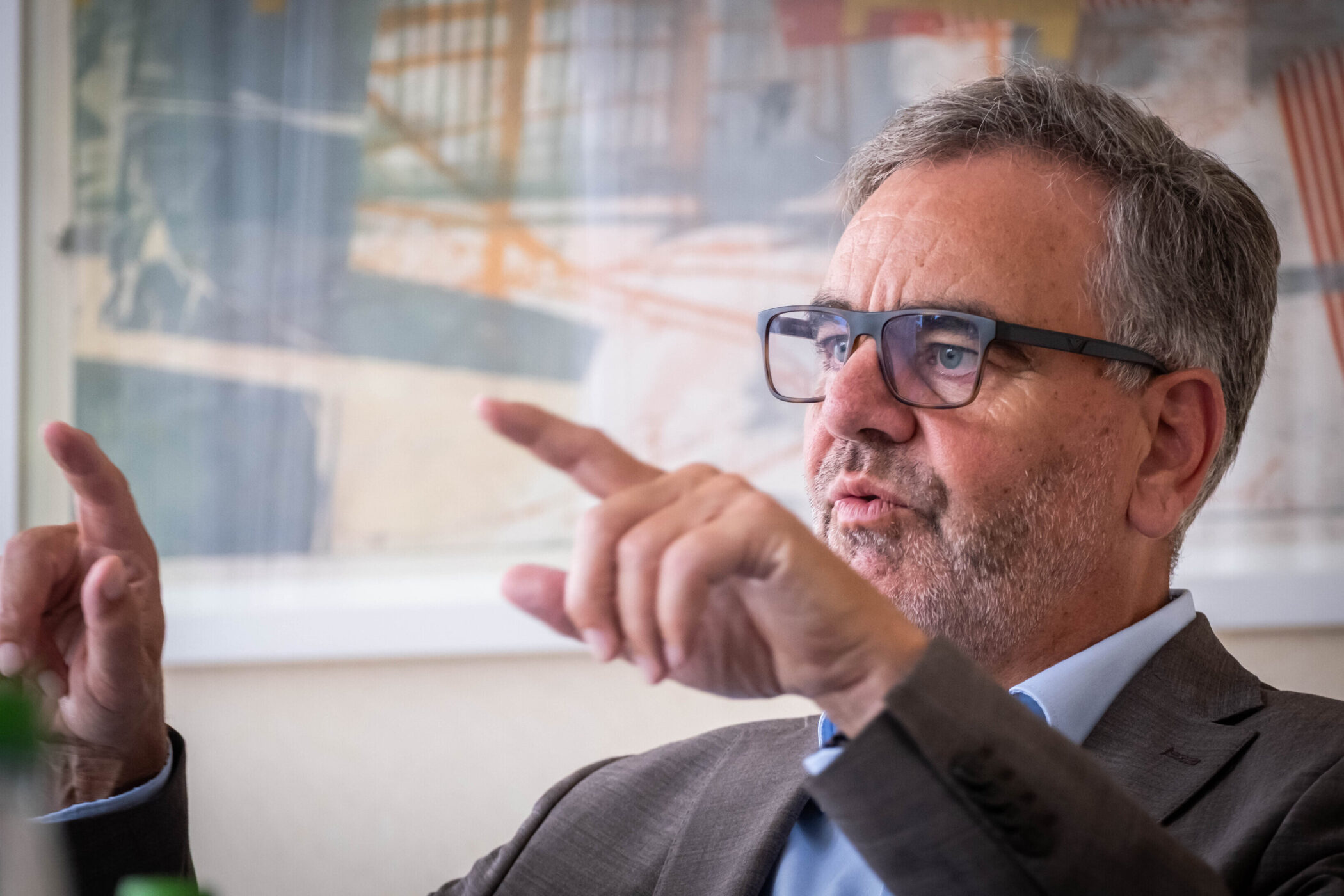 Mann mit Brille gestikuliert, unscharfer Hintergrund mit Kunstwerk.