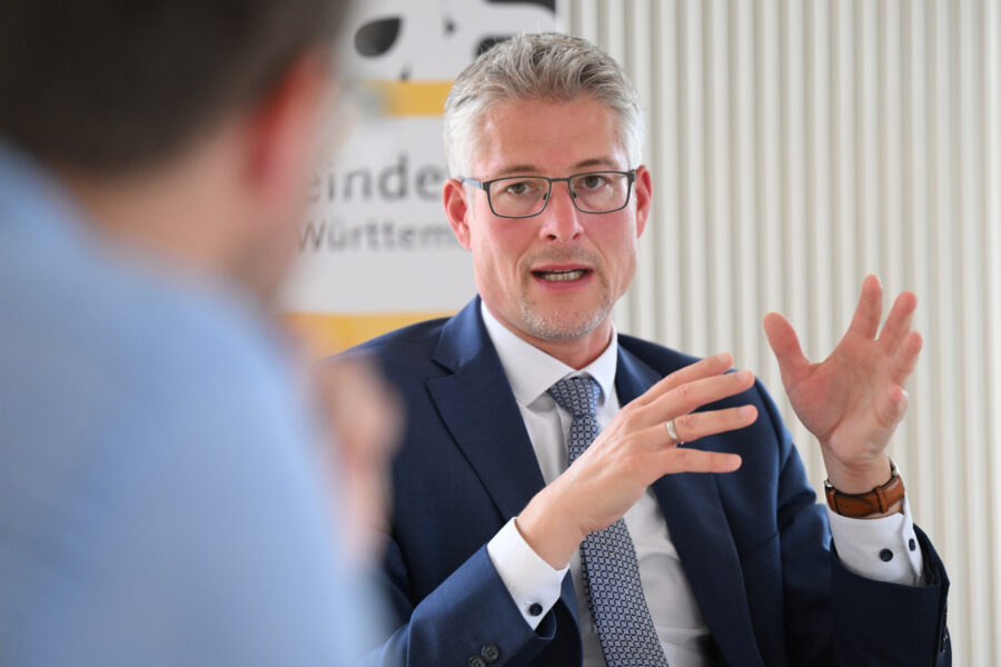 Zwei Männer im Gespräch, einer gestikuliert, trägt Anzug und Brille.