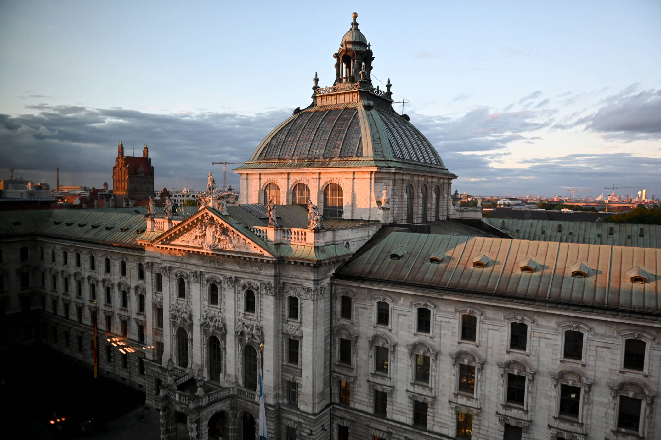 Historisches Gebäude mit Kuppel, beleuchtet von der Abendsonne, im Hintergrund Stadtansicht.