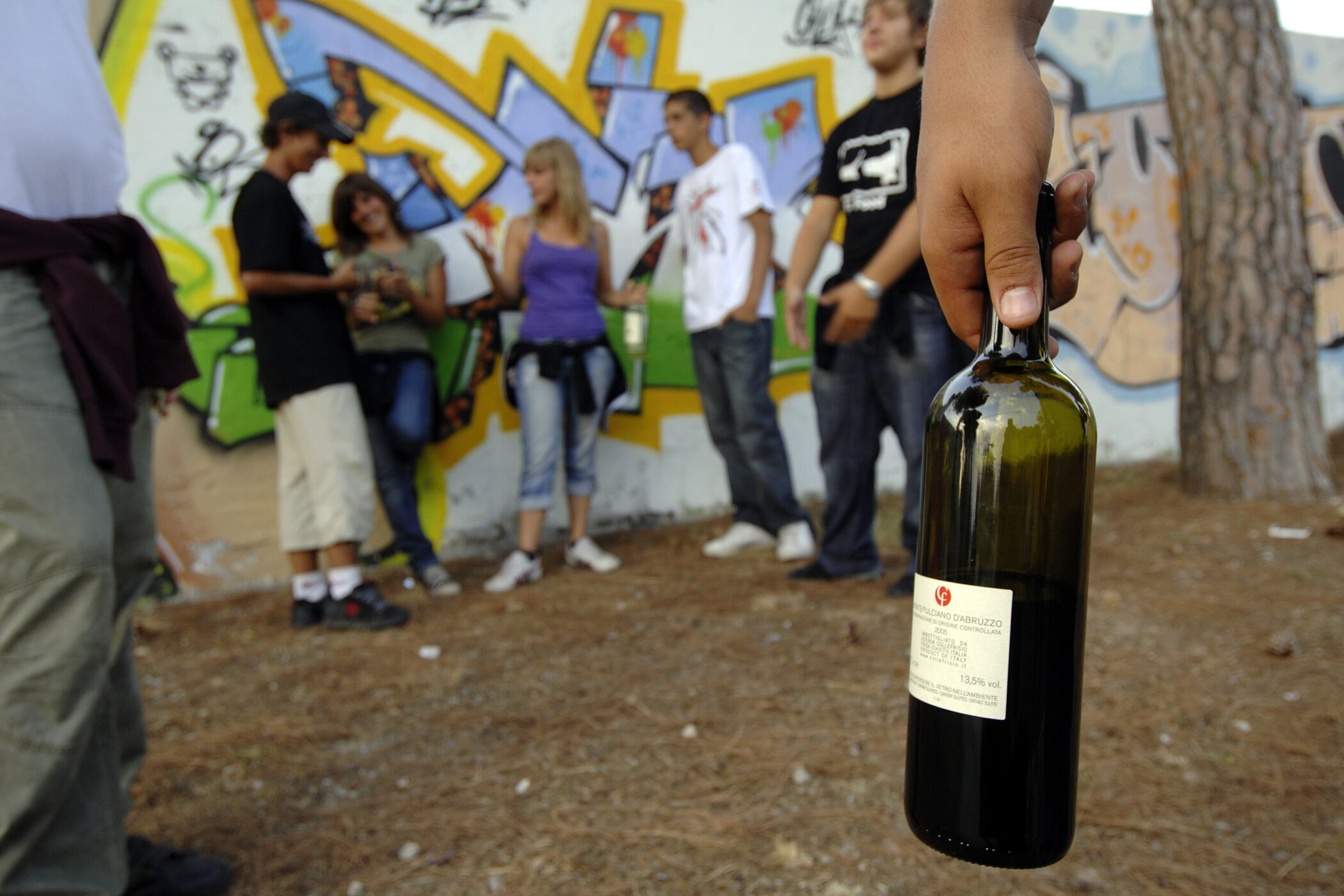 Fünf Personen vor einer Graffiti-Wand, eine hält eine Flasche.