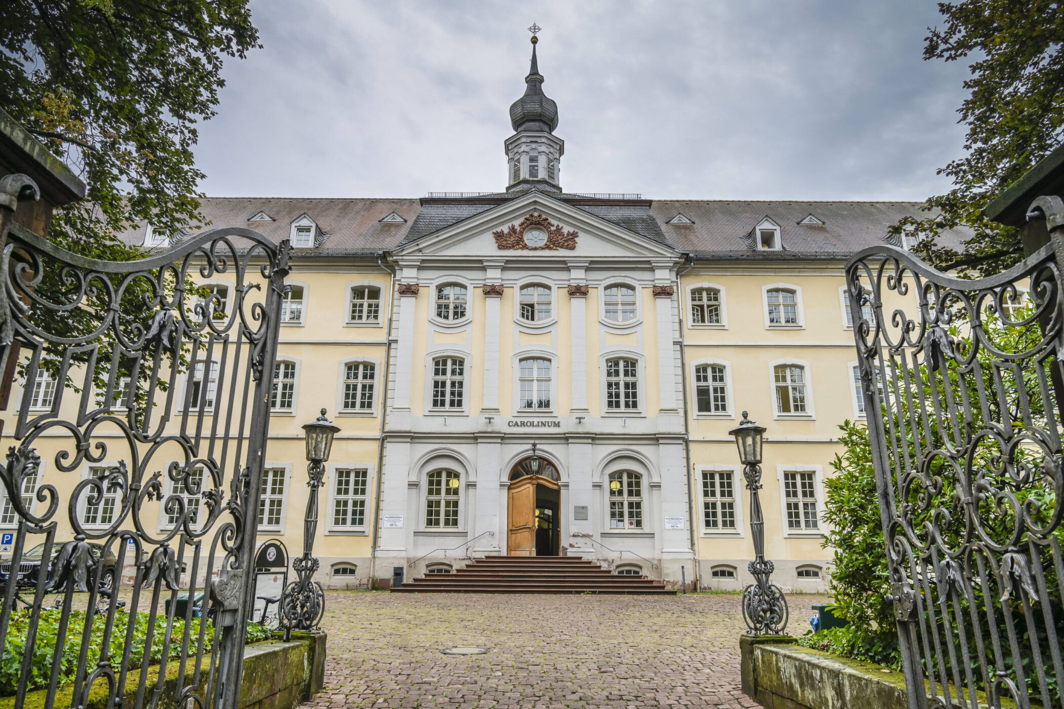 Historisches Gebäude mit Turm, schmiedeeisernes Tor im Vordergrund.