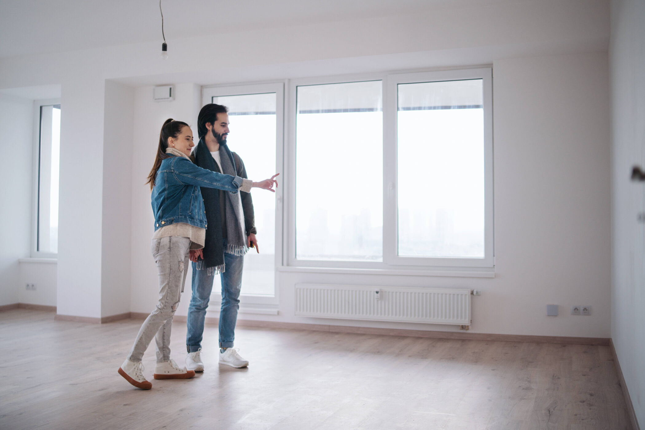 Zwei Personen in leerem Raum mit großen Fenstern, eine zeigt auf etwas.