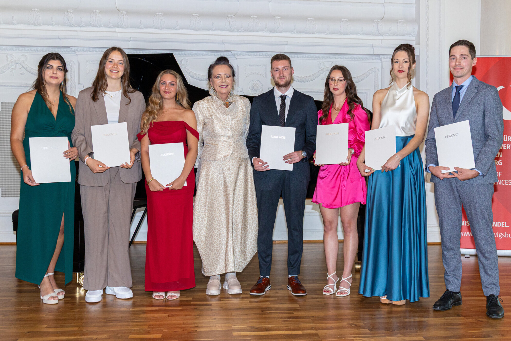 Acht Personen stehen nebeneinander, halten Urkunden in den Händen.