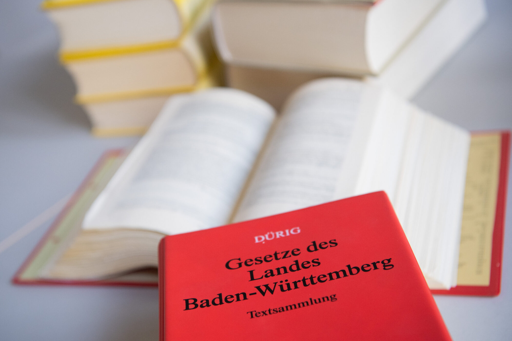 Rotes Buch mit Aufschrift "Gesetze des Landes Baden-Württemberg", offene Bücher im Hintergrund.