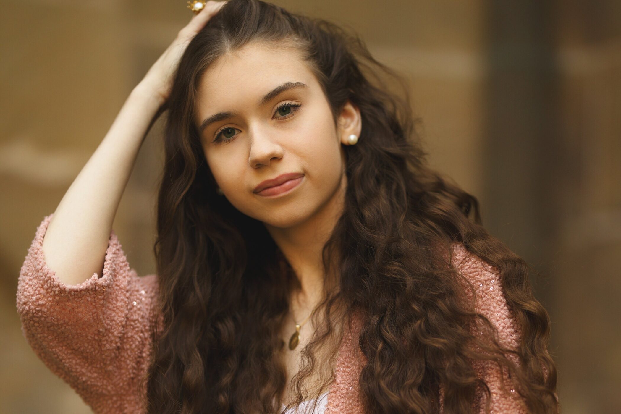 Junge Frau mit langen, lockigen Haaren, trägt rosa Oberteil, schaut in die Kamera.