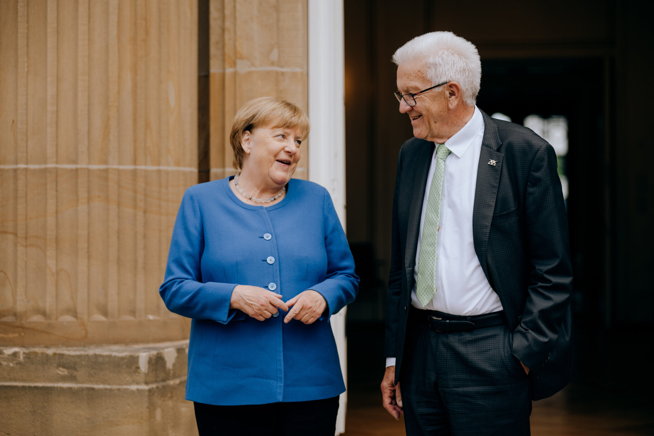 Zwei Personen im Gespräch vor einem Gebäude. Eine trägt ein blaues Oberteil.