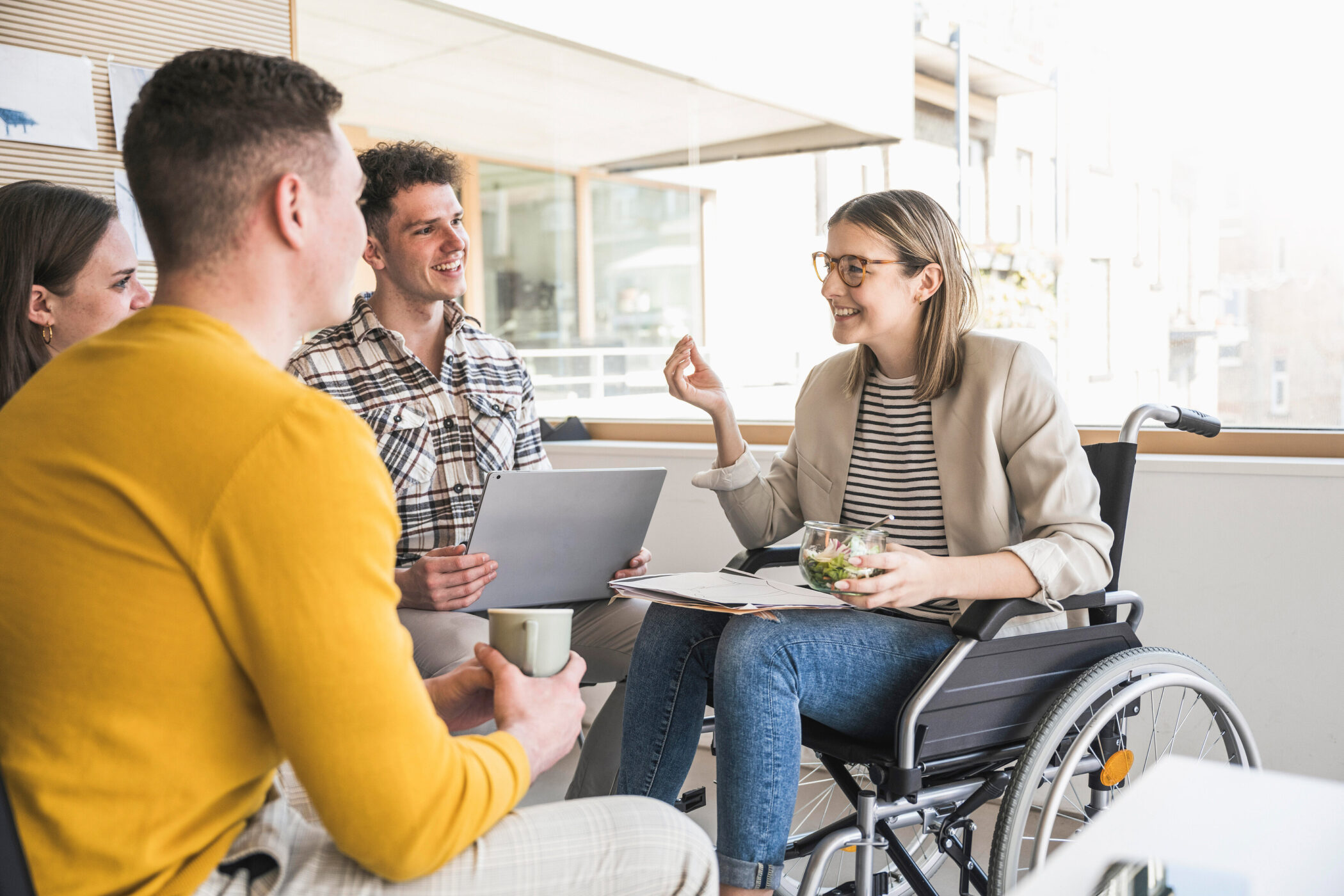 Vier Personen im Gespräch, eine Person im Rollstuhl mit Salatschüssel.