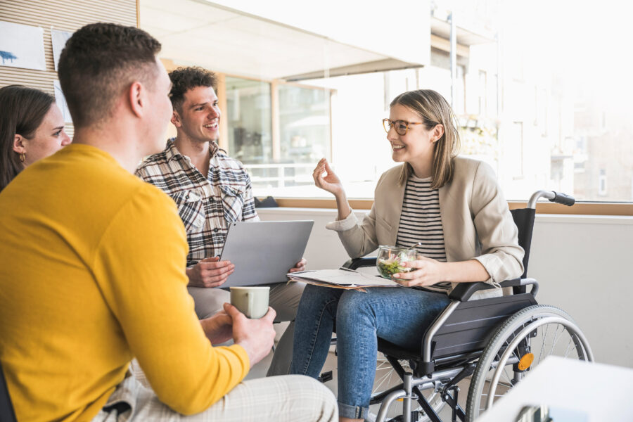 Vier Personen im Gespräch, eine Person im Rollstuhl mit Salatschüssel.