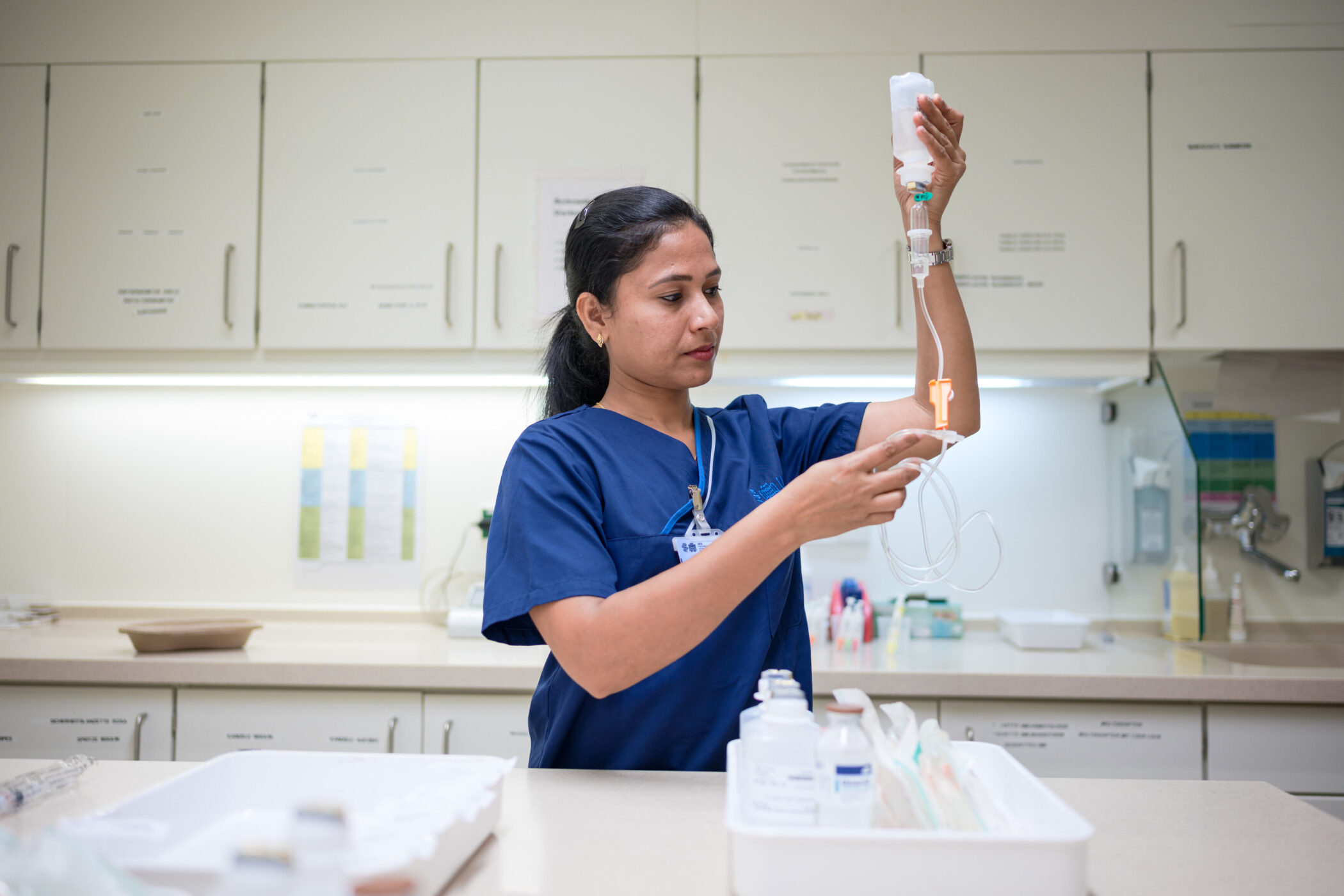 Person in blauer Kleidung hält Infusionsbeutel in einem medizinischen Raum.