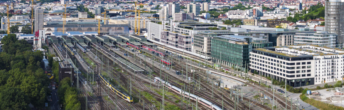 Bahnhof mit mehreren Gleisen, Zügen und umgebenden Gebäuden in einer Stadtlandschaft.