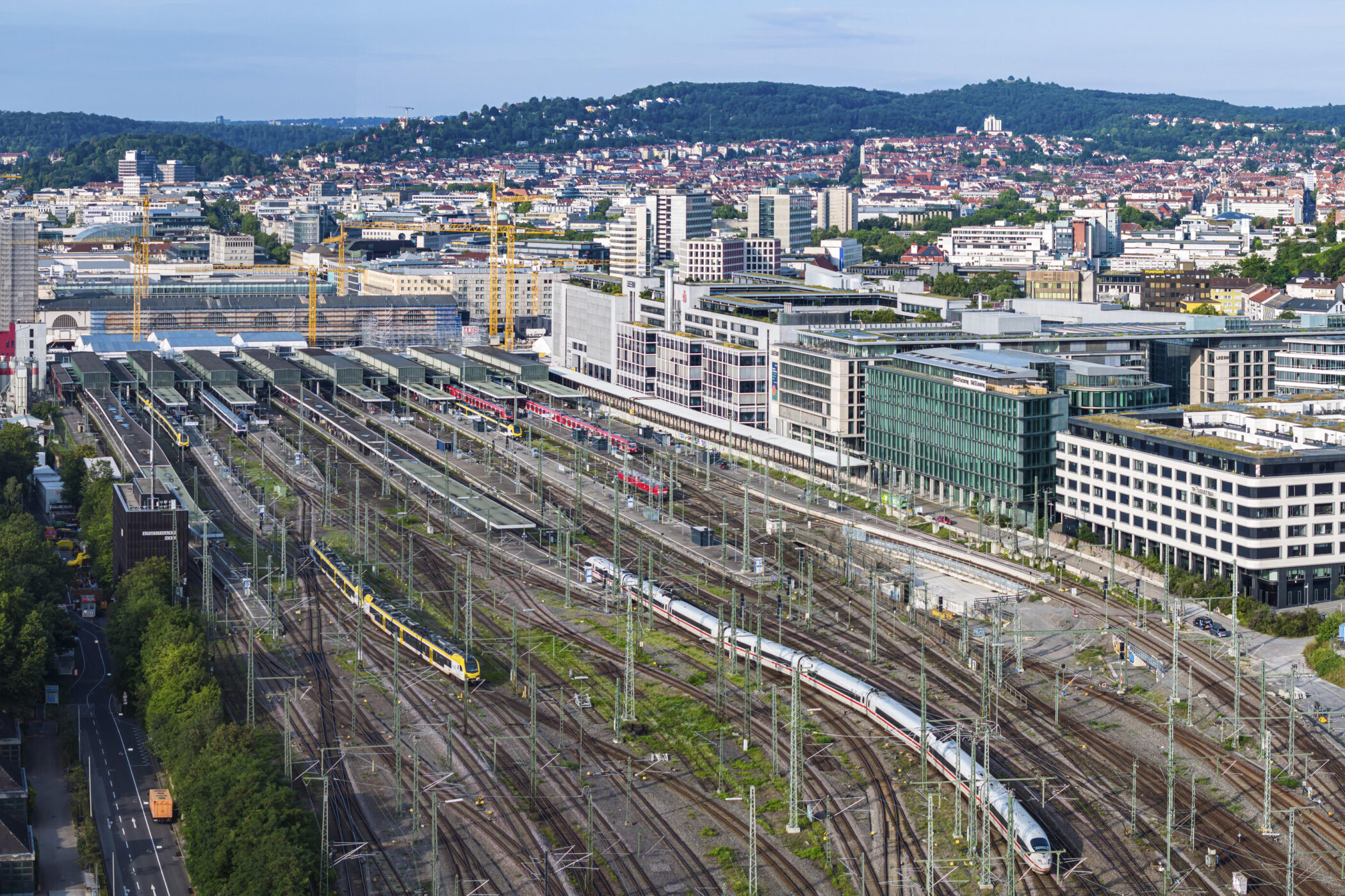 Bahnhof mit mehreren Gleisen, Zügen und umgebenden Gebäuden in einer Stadtlandschaft.
