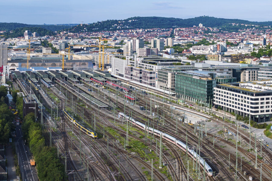 Bahnhof mit mehreren Gleisen, Zügen und umgebenden Gebäuden in einer Stadtlandschaft.