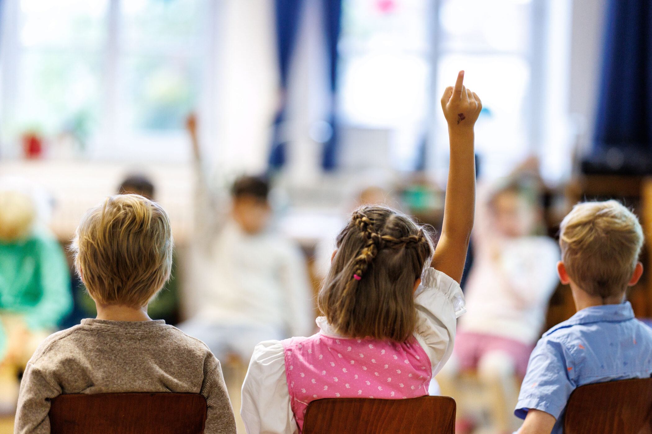 Kinder sitzen in einem Klassenzimmer, eines hebt die Hand.
