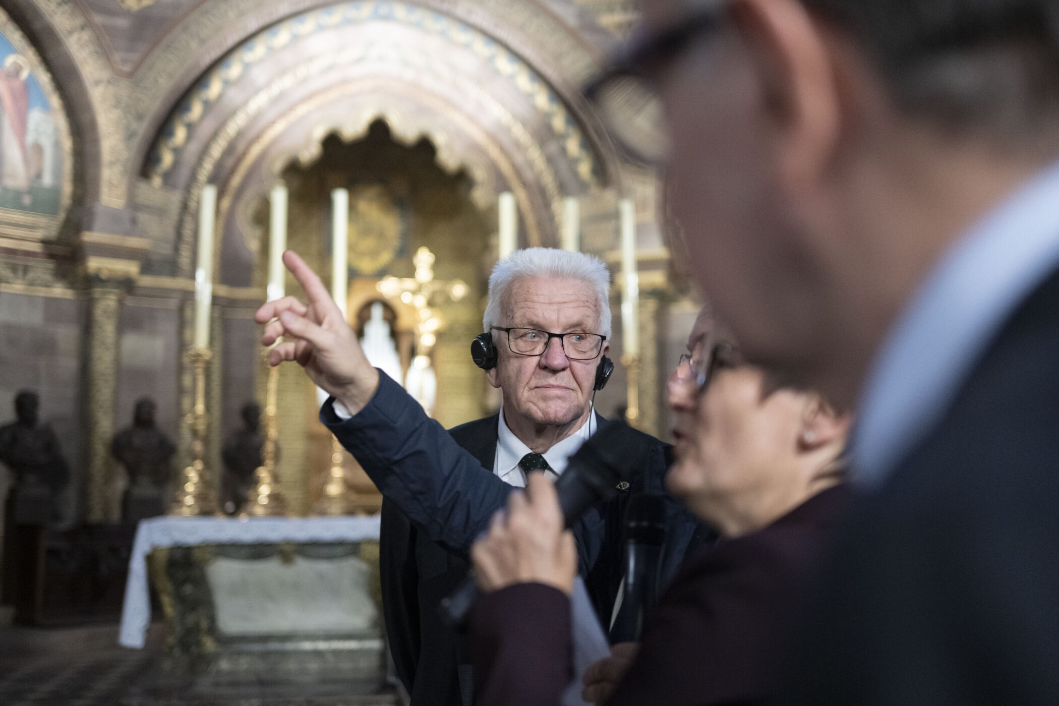 Drei Personen in einer Kirche, eine zeigt mit dem Finger, eine trägt Kopfhörer.