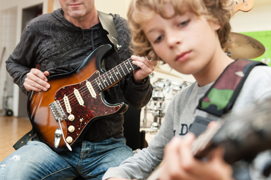 Zwei Personen spielen E-Gitarren, eine sitzt, die andere steht.