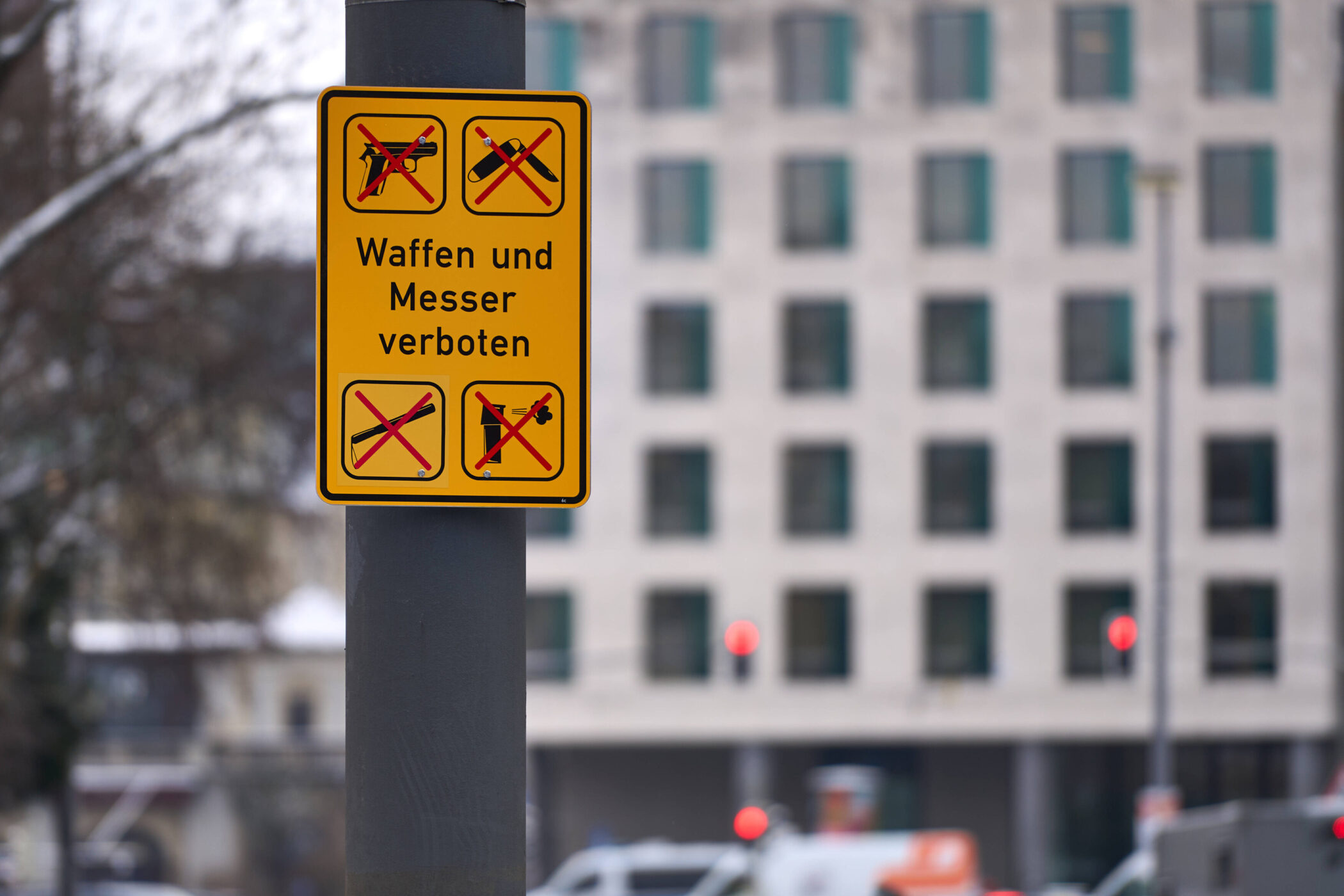Gelbes Schild mit durchgestrichenen Waffen und Text: "Waffen und Messer verboten".