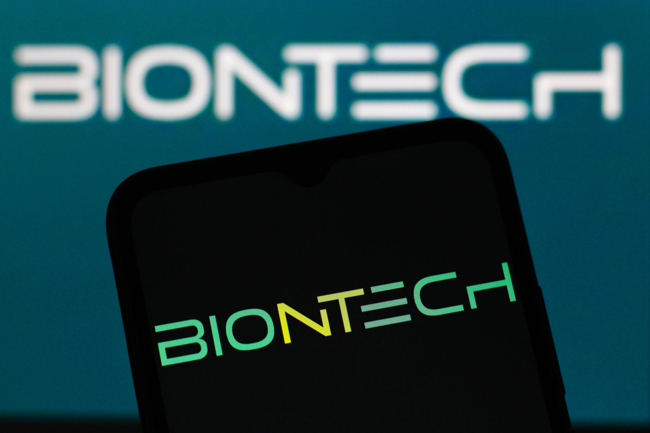 Zwei "BIONTECH"-Logos auf Bildschirm und Smartphone.