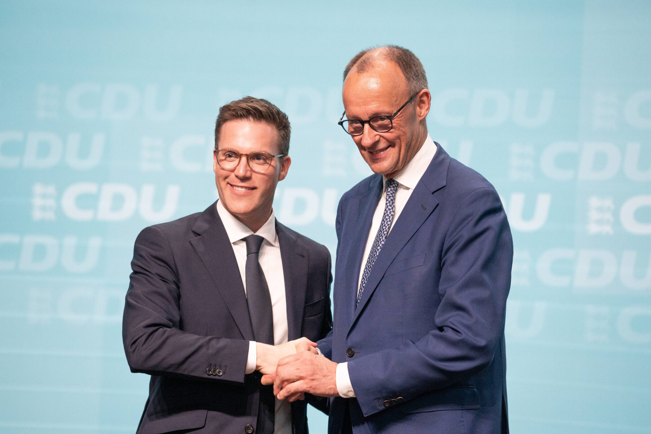 Zwei Männer im Anzug schütteln sich die Hand vor CDU-Logo.