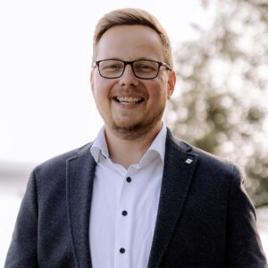 Lächelnder Mann mit Brille und Anzug im Freien.