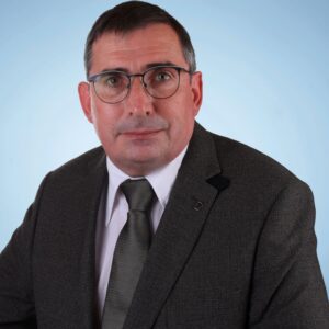 Mann mit Brille und Anzug vor blauem Hintergrund.