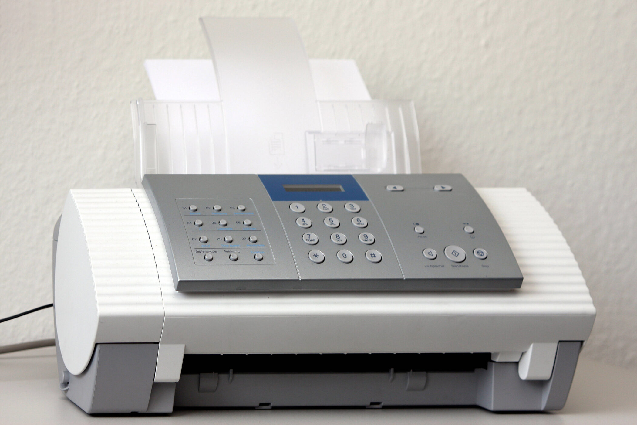 Faxgerät mit Tastenfeld und eingelegtem Papier auf einem Tisch.