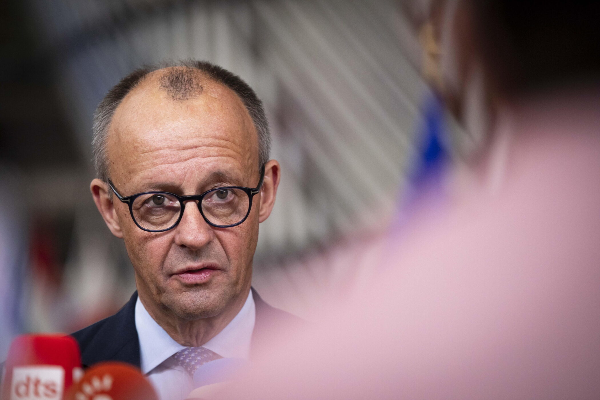 Ein Mann mit Brille spricht vor Mikrofonen.